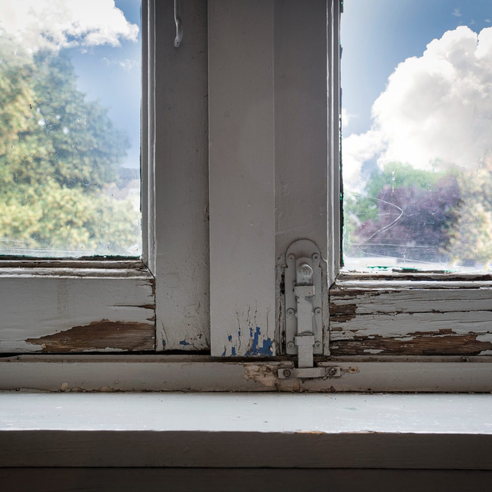 Old wooden window frames with rotting wood and cracked peeling paint, house needs renovation and new frames closeup